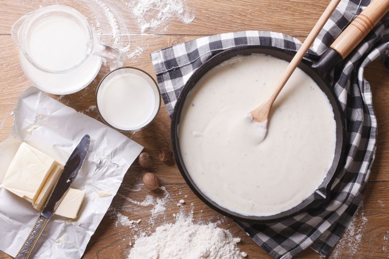 Table with flour and dairy ingredients and a pan with a  pancake mixture